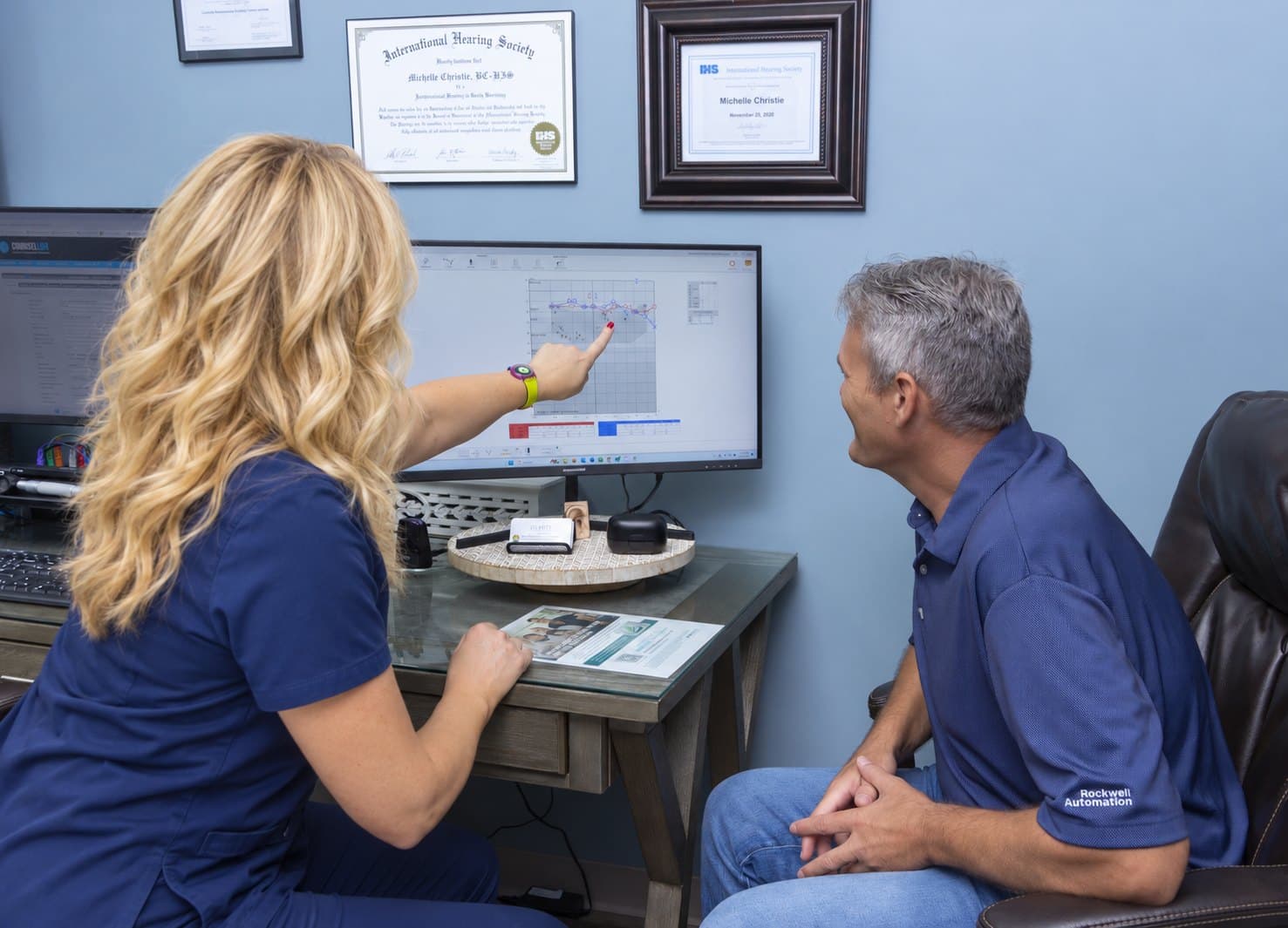 Michelle pointing to a hearing test result on screen as a patient listens