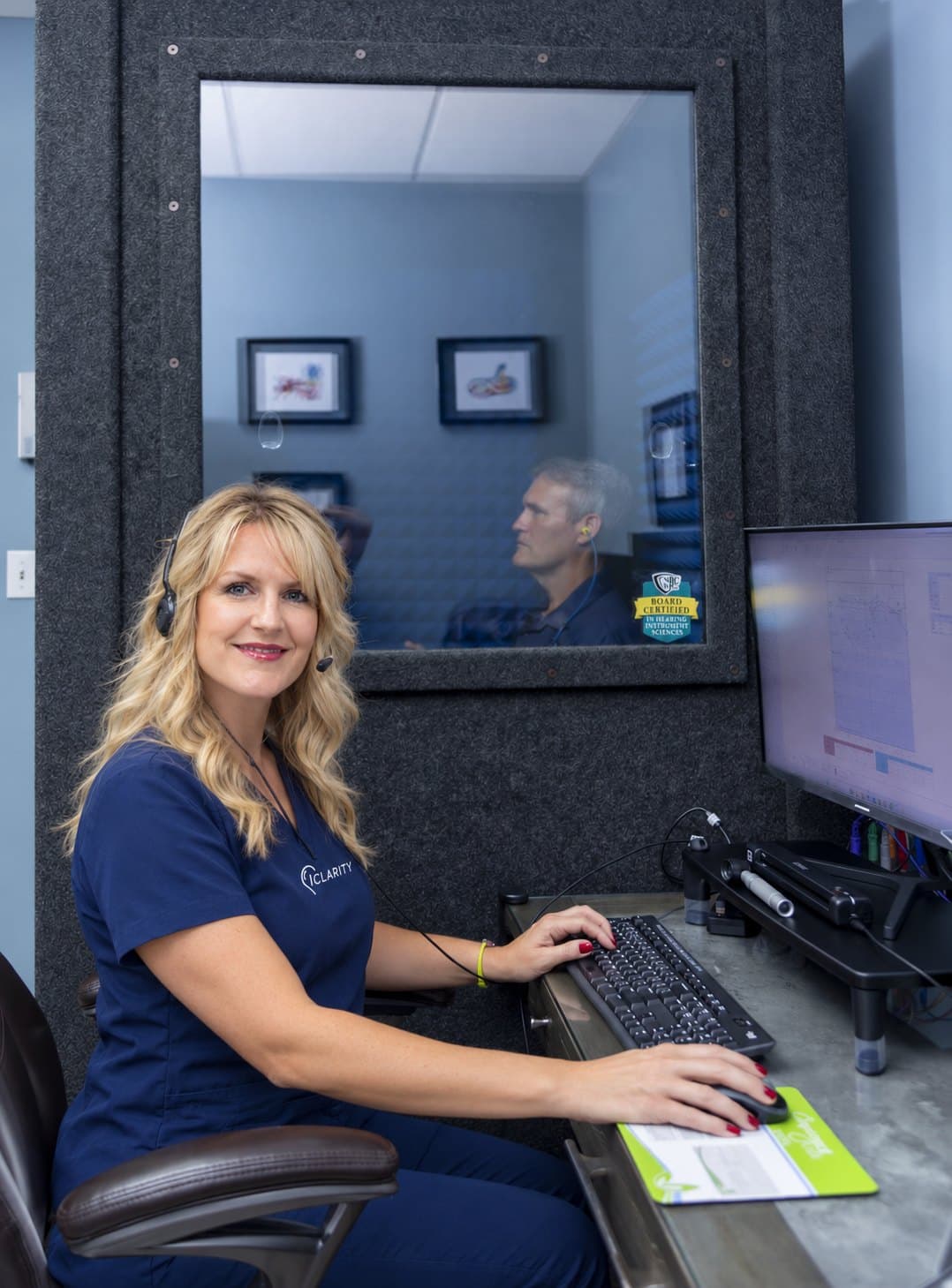Michelle at the audiometer while a patient sits in the sound booth
